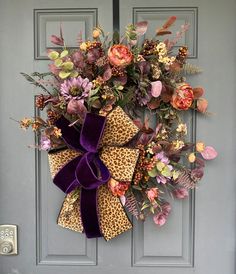 a leopard print wreath with purple velvet bow hanging on the front door, decorated with flowers and foliage