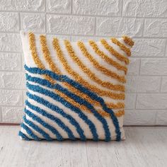 a blue and yellow striped pillow sitting on top of a white brick wall next to a wooden floor