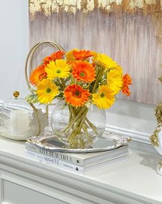 a vase filled with yellow and orange flowers sitting on top of a white dresser next to a mirror