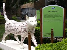 a white cat statue sitting on top of a block of land next to a sign