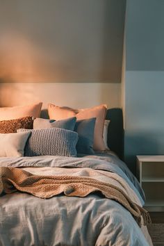 a bed with pillows and blankets on top of it next to a night stand in front of a wall