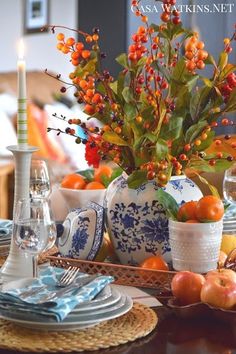 the table is set with blue and white dishes, silverware, oranges and berries