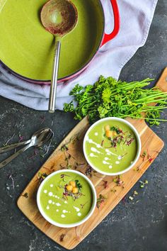 two bowls filled with green soup on top of a cutting board