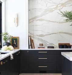 a kitchen with marble counter tops and black cabinets, along with white flowers in vases