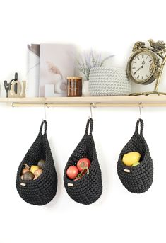 three bags hanging on the wall with fruit and vegetables in them next to a clock