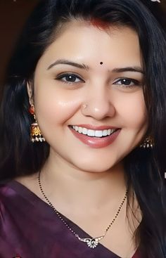 a woman with long black hair smiling at the camera and wearing earrings on her head