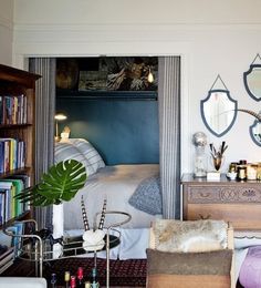 a living room filled with furniture and bookshelves next to a bed covered in blankets