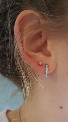 a close up of a person's ear with two small diamond earrings on it