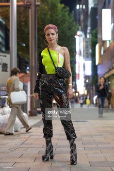 a woman with pink hair wearing black pants and neon top standing on the side walk