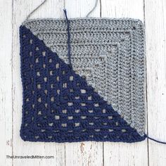 a crocheted square is hanging on a white wooden surface with blue and gray yarn