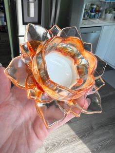 a hand holding an orange flower shaped glass candle holder