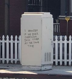 a white box sitting on the side of a road next to a white picket fence