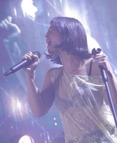 a woman holding a microphone in her right hand and singing into the microphone on stage