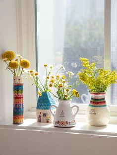 three vases filled with flowers sitting on a window sill next to each other