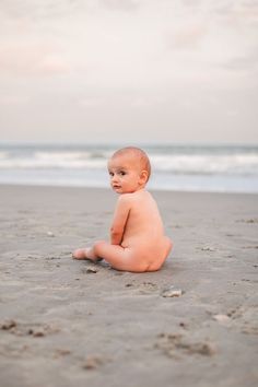 a baby sitting in the sand at the beach