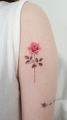 a pink rose tattoo on the left arm and shoulder, with small leaves around it