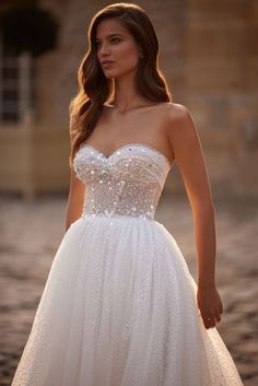 a woman in a white wedding dress standing on a cobblestone street at sunset