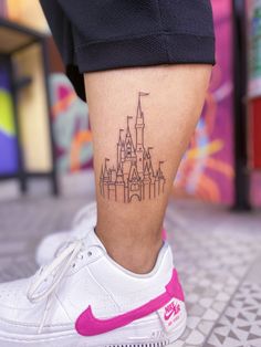 a woman's leg with a tattoo on it that has a castle in the background