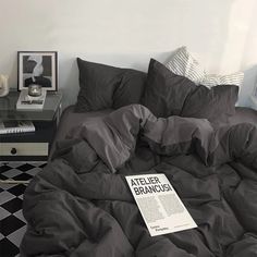 a black and white bedroom with a large bed covered in grey sheets, pillows and blankets