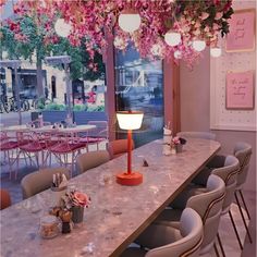 a long table with many chairs around it and a lamp in the center surrounded by pink flowers