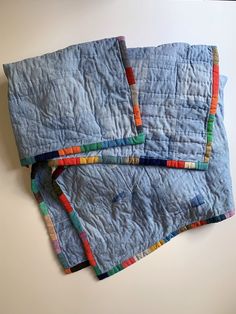 three pieces of blue quilt sitting on top of a white tablecloth covered in multicolored strips