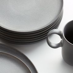 a stack of gray plates and cups on top of a white tablecloth with a black coffee cup in the middle