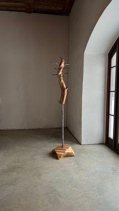 a wooden sculpture sitting on top of a metal pole in an empty room next to a window