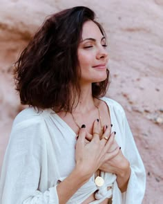 a woman standing in front of a rock formation with her hands clasped to her chest