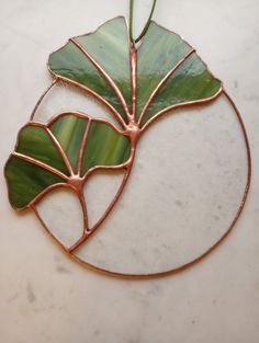 a piece of art made out of copper wire and green leaves on a marble surface