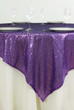 the table is covered with purple sequins and place settings for four wine glasses