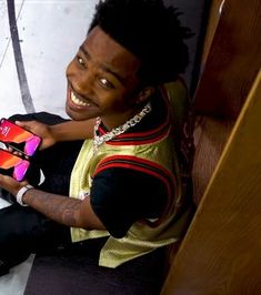 a young man sitting on the floor holding a cell phone in his hand and smiling