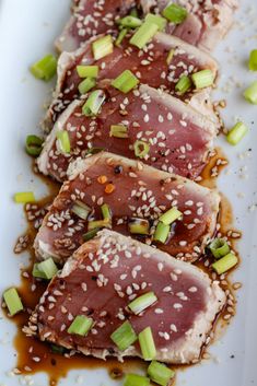 three pieces of meat on a white plate with sesame seeds and green onions sprinkled around it