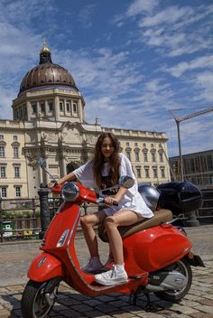 a woman sitting on top of a red scooter in front of a building