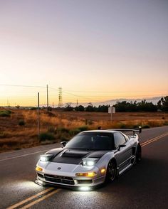 a silver sports car driving down the road at sunset with its hood up and lights on