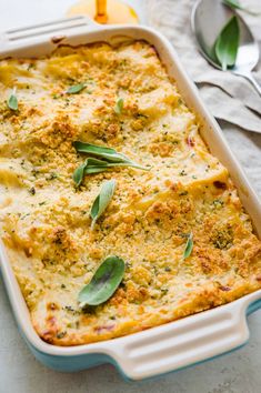 a casserole dish with cheese and herbs in it on a table next to spoons