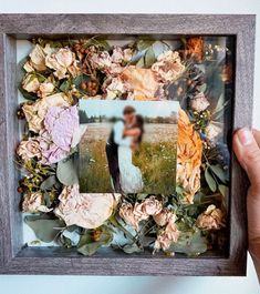 a person holding up a wooden frame with flowers on it