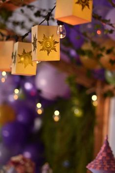 some paper lanterns hanging from a tree with purple and yellow balloons in the back ground