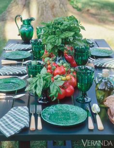 a table set with green plates, silverware and fresh vegetables is shown in front of a tree