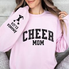 "Elevate your cheer mom style with our cozy and customizable Cheer Mom Sweatshirt! Crafted for comfort and designed for the ultimate cheer supporter, this sweatshirt is a must-have for chilly game days and spirited practices. Key Features: Soft and warm fleece lining for maximum comfort. Stylish \"Cheer Mom\" design on the front to showcase your pride. Personalize the sleeve with your kids' names for a truly unique touch. Available in various sizes to ensure a perfect fit. Why Choose Our Cheer M Cheerleading Letter Print Crew Neck Sweatshirt, Sporty Cheerleading Tops With Name Print, Crew Neck Sweatshirt With Letter Print For Cheerleading, Letter Print Sweatshirt For Cheerleading, Cotton Sweatshirt With Letter Print For Cheerleading, Collegiate Customizable Tops For Cheerleading, Collegiate Cheerleading Customizable Tops, Customizable Crew Neck Sweatshirt For Cheerleading, Pink Long Sleeve Tops For Cheerleading