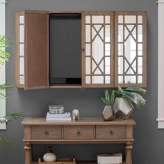 a wooden cabinet with two doors and some books on it next to a potted plant