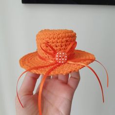 a hand holding an orange crocheted hat with a button on the side and ribbon around the brim