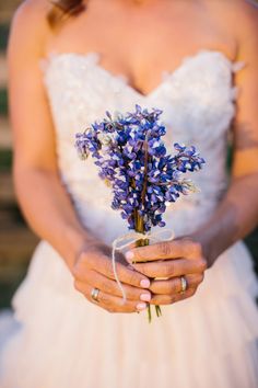 a woman in a wedding dress holding a bouquet of purple flowers with her hands wrapped around it