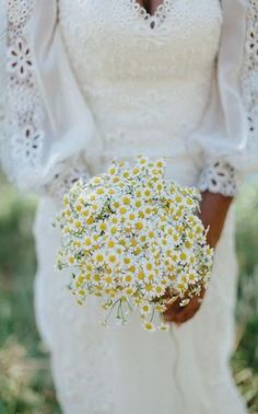 a woman in a white dress holding a bouquet of daisies on her wedding day