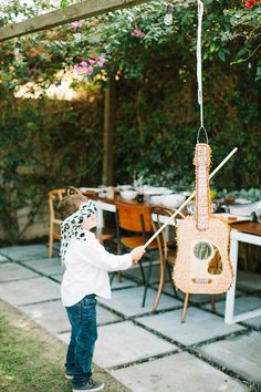 a little boy playing with a toy guitar hanging from a string on a patio table