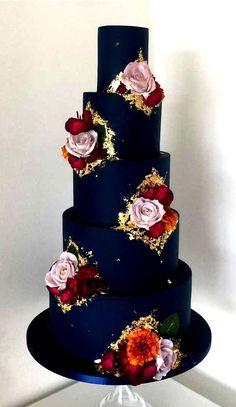 a three tiered blue wedding cake with flowers on the side and gold sprinkles