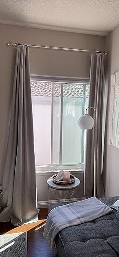 a bed sitting in a bedroom next to a window with curtains on the windowsill