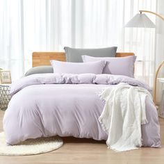 a bed with purple comforter and pillows in a room next to a white rug