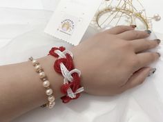 a woman's hand wearing a red and white bracelet with pearls on the wrist