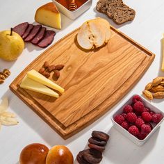 a wooden cutting board topped with lots of different types of food next to fruit and nuts