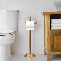 a white toilet sitting next to a wooden cabinet with towels on it's rack